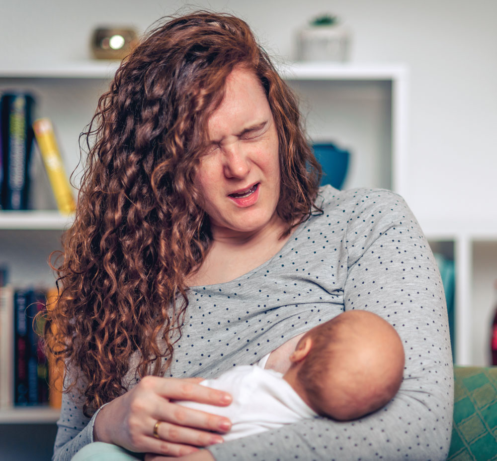 Mother wincing in discomfort while breastfeeding her baby