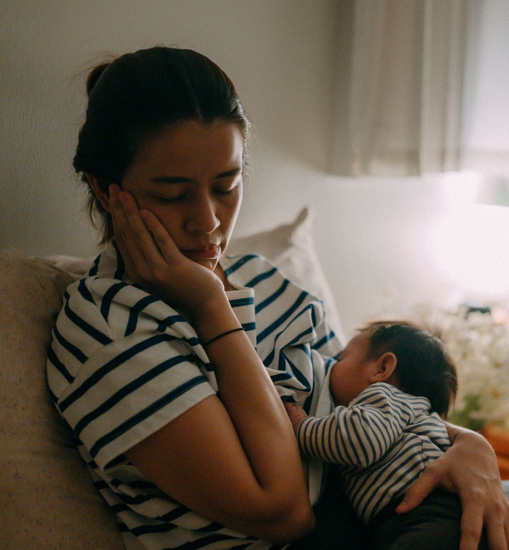 Tired mother breastfeeding baby in striped shirt