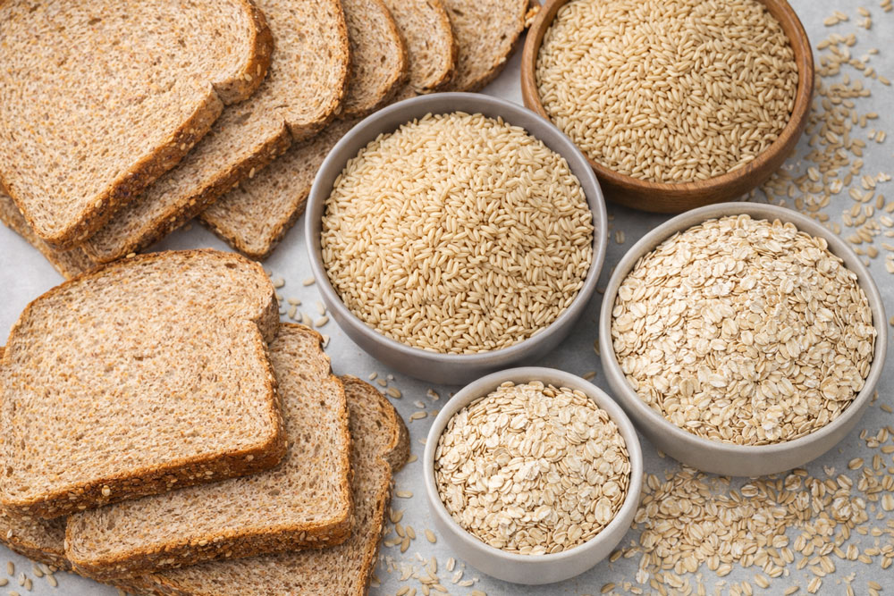 Three bowls contain quinoa, brown rice, and oats