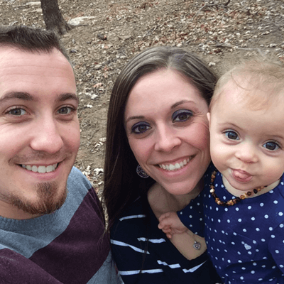 Smiling family of three outdoors, baby sticking tongue out