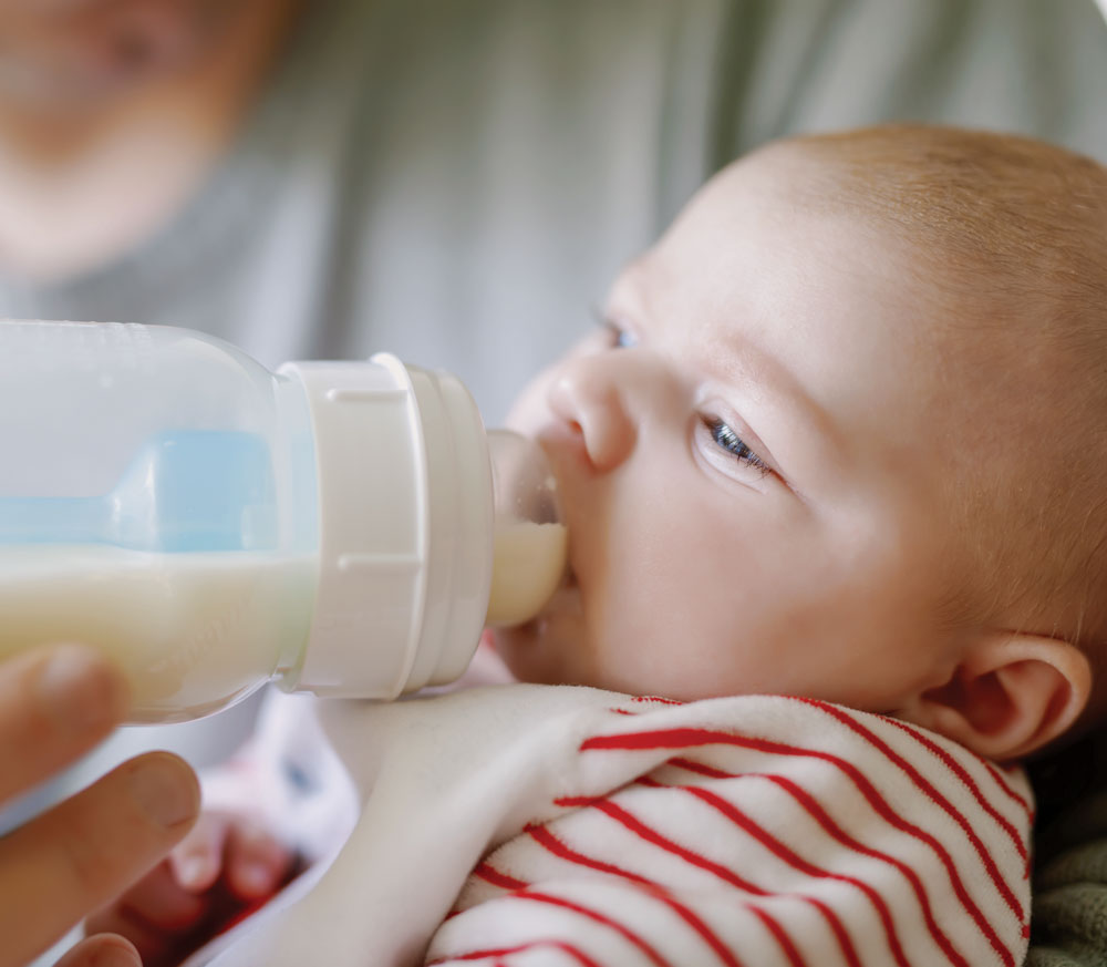 Baby drinking milk from a bottle, wearing striped outfit