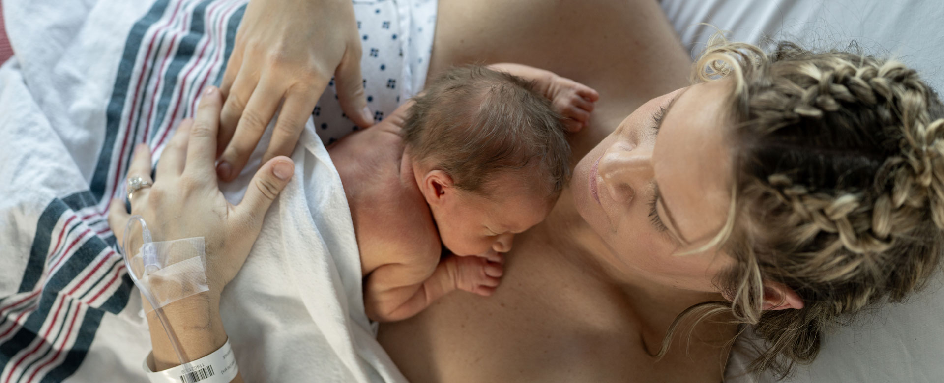 Mother holding newborn skin to skin in hospital bed