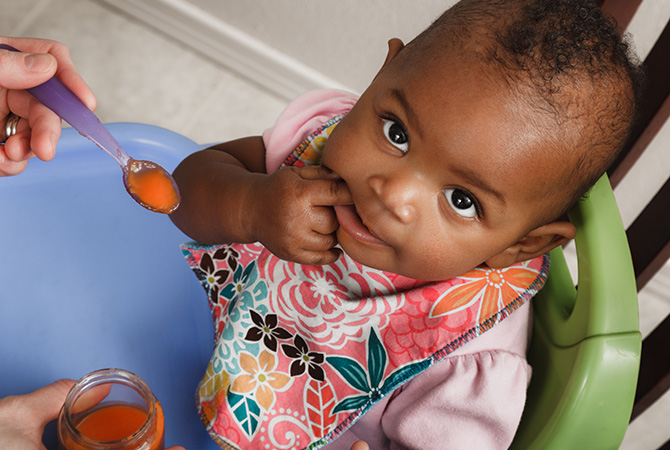 Baby eating with spoon, wearing colorful bib.