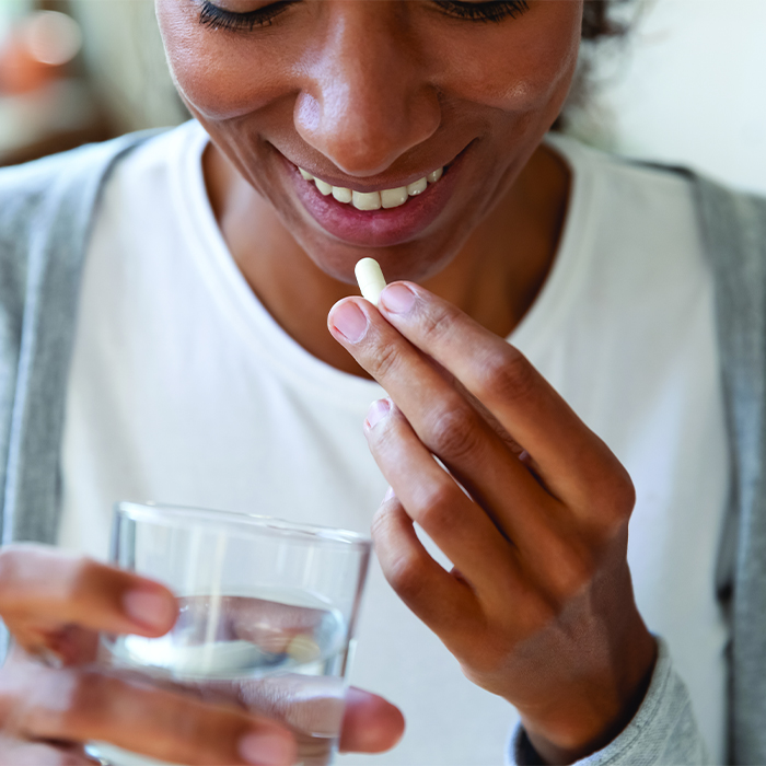 Woman smiling, holding pill and glass of water