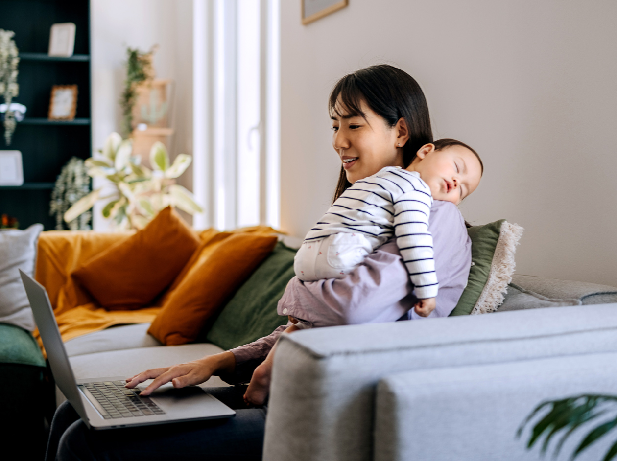 Woman using laptop while holding sleeping baby