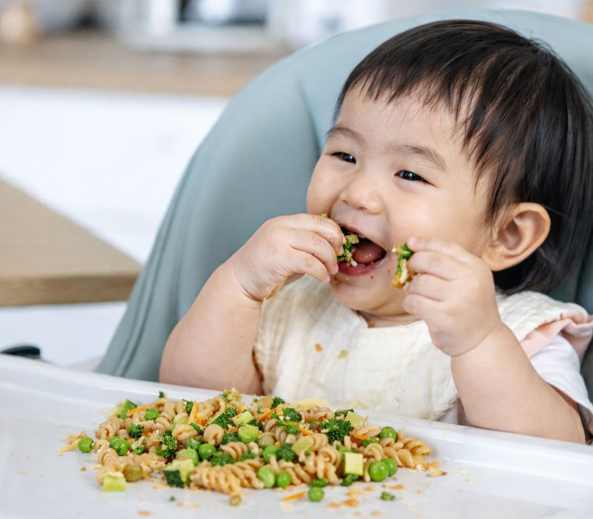 Baby eating pasta with vegetables