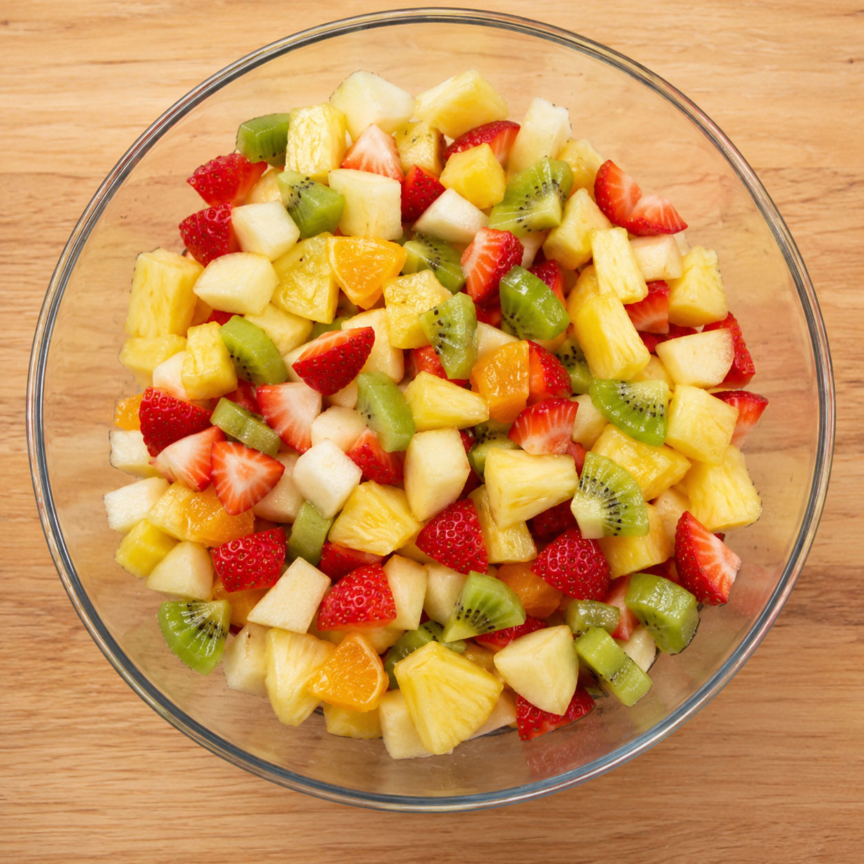 Chopped mixed fruit in glass bowl on wooden table