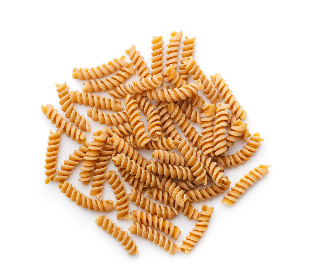 Whole wheat fusilli pasta piled on white background
