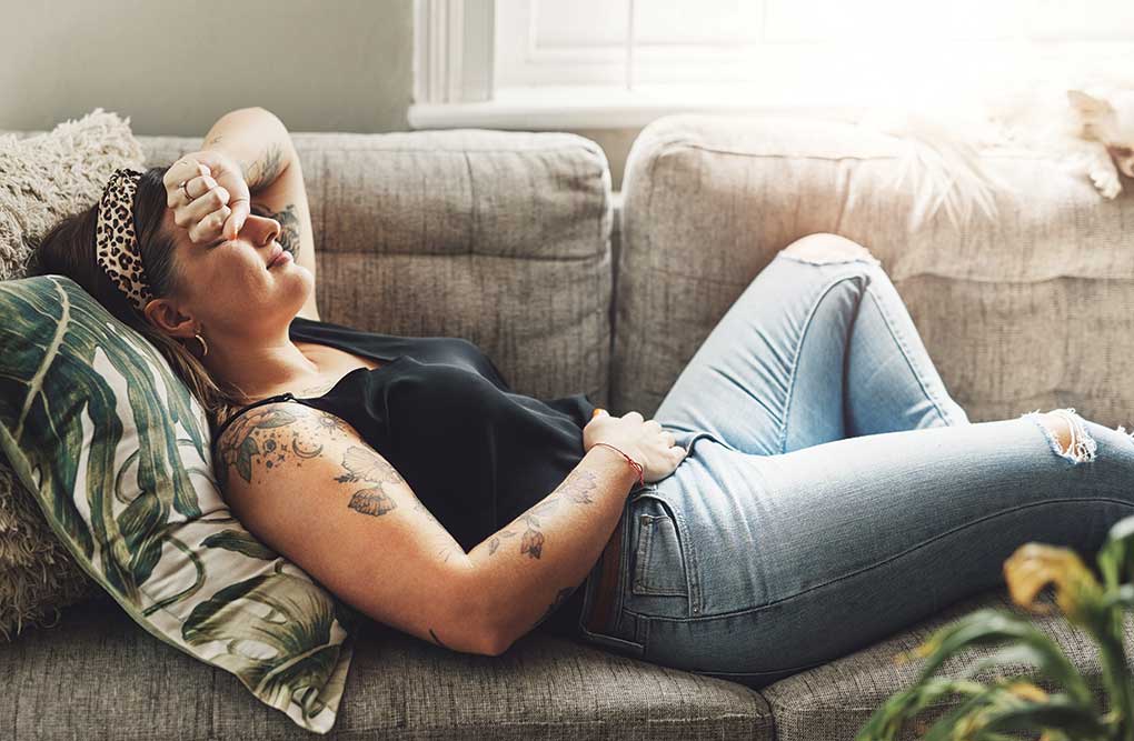 Woman resting on a couch holding her head, appearing unwell and tired