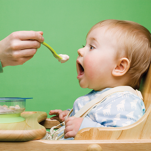 Baby in high chair being fed with a spoon.