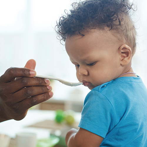 Adult hand feeding a young child with a spoon.