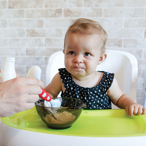 Baby in a high chair eating with a spoon.